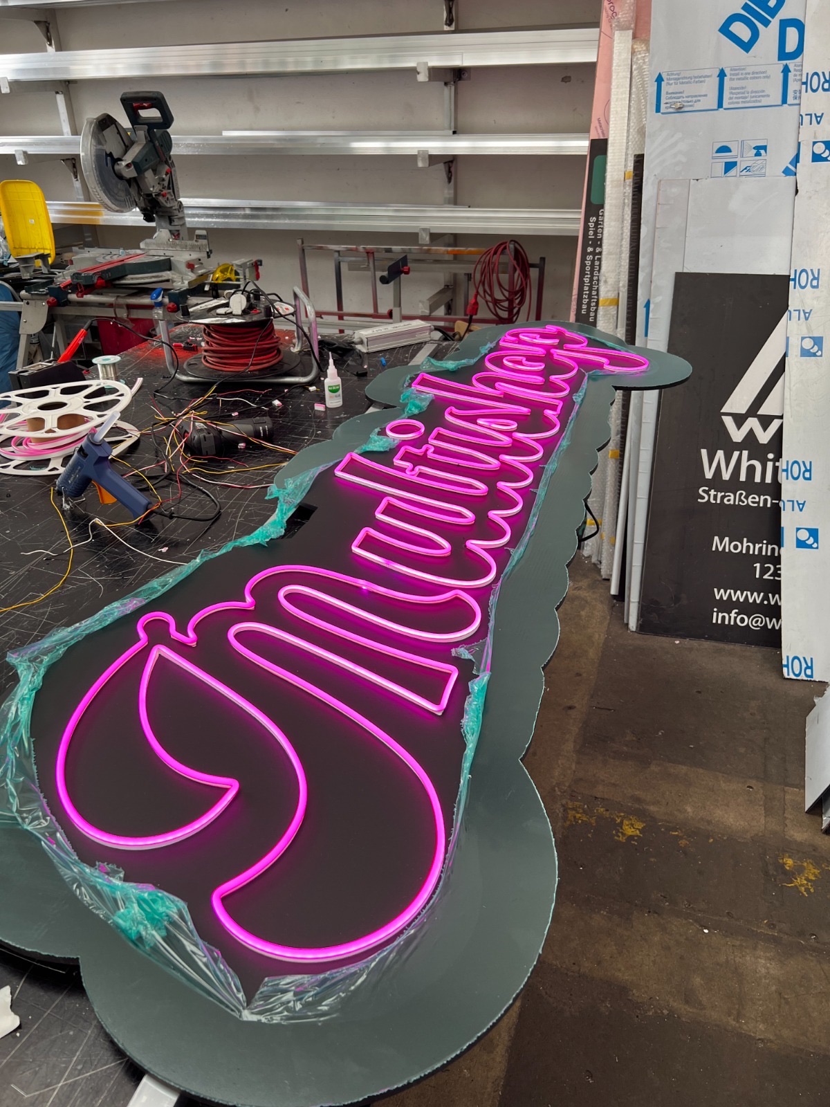 Pinker LED-Neon-Schriftzug in Schreibschrift auf einer Trägerplatte in der Goldblick-Werkstatt
